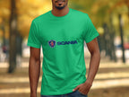 Clad in a green cotton T-shirt featuring Scanias blue logo, a person stands outdoors. The autumn foliage of out-of-focus trees provides a warm backdrop as one hand rests casually in their jeans pocket, perfectly embodying the relaxed charm of Garment Graphics merchandise.