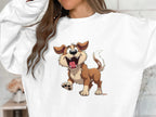 A woman in a cozy, white Garment Graphics sweatshirt showcases a playful, animated dog with brown fur, a red collar, and a wagging tail—ideal for dog lovers. Her long brown hair and raised arms enhance the joyful vibe.
