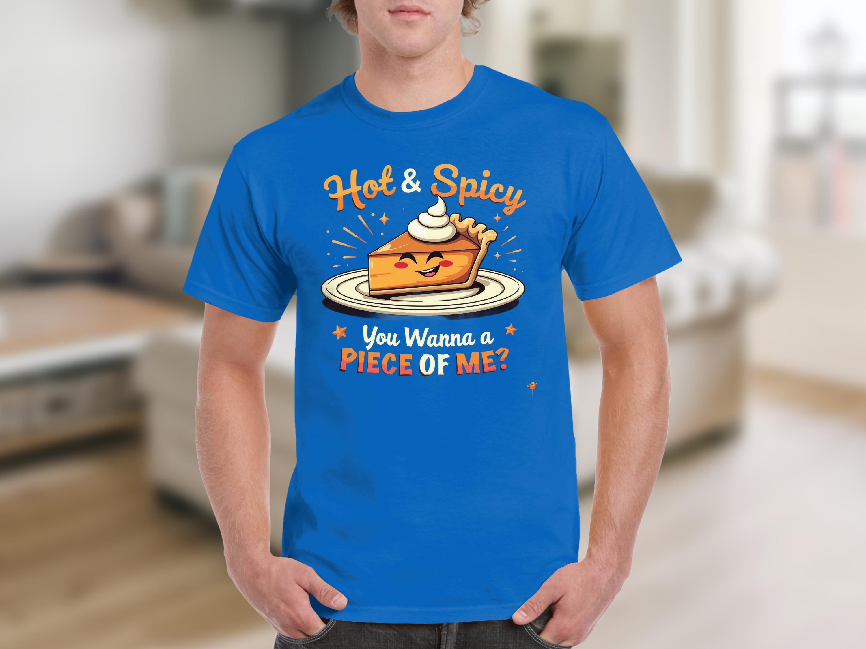 A person is wearing a Garment Graphics blue T-shirt with a Hot and Spicy Pie Design, showcasing a pie slice topped with whipped cream. The shirt says, You Wanna a Piece of Me? The backdrop is a blurred indoor scene.