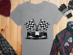 Garment Graphics gray T-shirt showcases a black-and-white race car with crossed checkered flags, ideal for motorsport fans. Its paired with a red plaid shirt, scarf, gloves, and maroon knit beanie on a wooden surface.