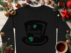 The Garment Graphics black sweatshirt, featuring a top hat with St Patricks Day and two green shamrocks, radiates festive flair amidst Christmas decor and a steaming coffee cup on wood.