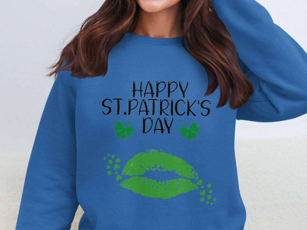 A woman embodies festive spirit in a blue Garment Graphics sweatshirt with Happy St. Patricks Day, two green shamrocks, and a bold clover kiss design. Her wavy brown hair frames her face as she gently touches the collar, radiating holiday cheer.