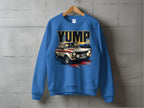 Garment Graphics blue sweatshirt showcases a bold YUMP rally car graphic with abstract lines, delivering a dynamic look. Displayed on a wooden hanger against a concrete wall, this piece combines vintage flair with modern style.