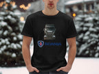 In a snowy setting, a person proudly wears a Garment Graphics black T-shirt loved by truck fans. It showcases an image of a Scania truck with its logo underneath. Standing with hands in pockets, they pose against snow-covered trees.