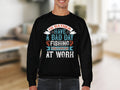 A person indoors wears a Garment Graphics black fishing sweatshirt, featuring vibrant designs and the text: Id rather have a bad day fishing than a good day at work. This comfy piece has unisex sizing for all fishing enthusiasts. The background is blurred.