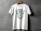 Garment Graphics offers a festive graphic T-shirt featuring a Happy St. Patricks Day design with a heart and shamrocks. It hangs stylishly on a wooden hanger against a gray backdrop, ready for celebration in style.
