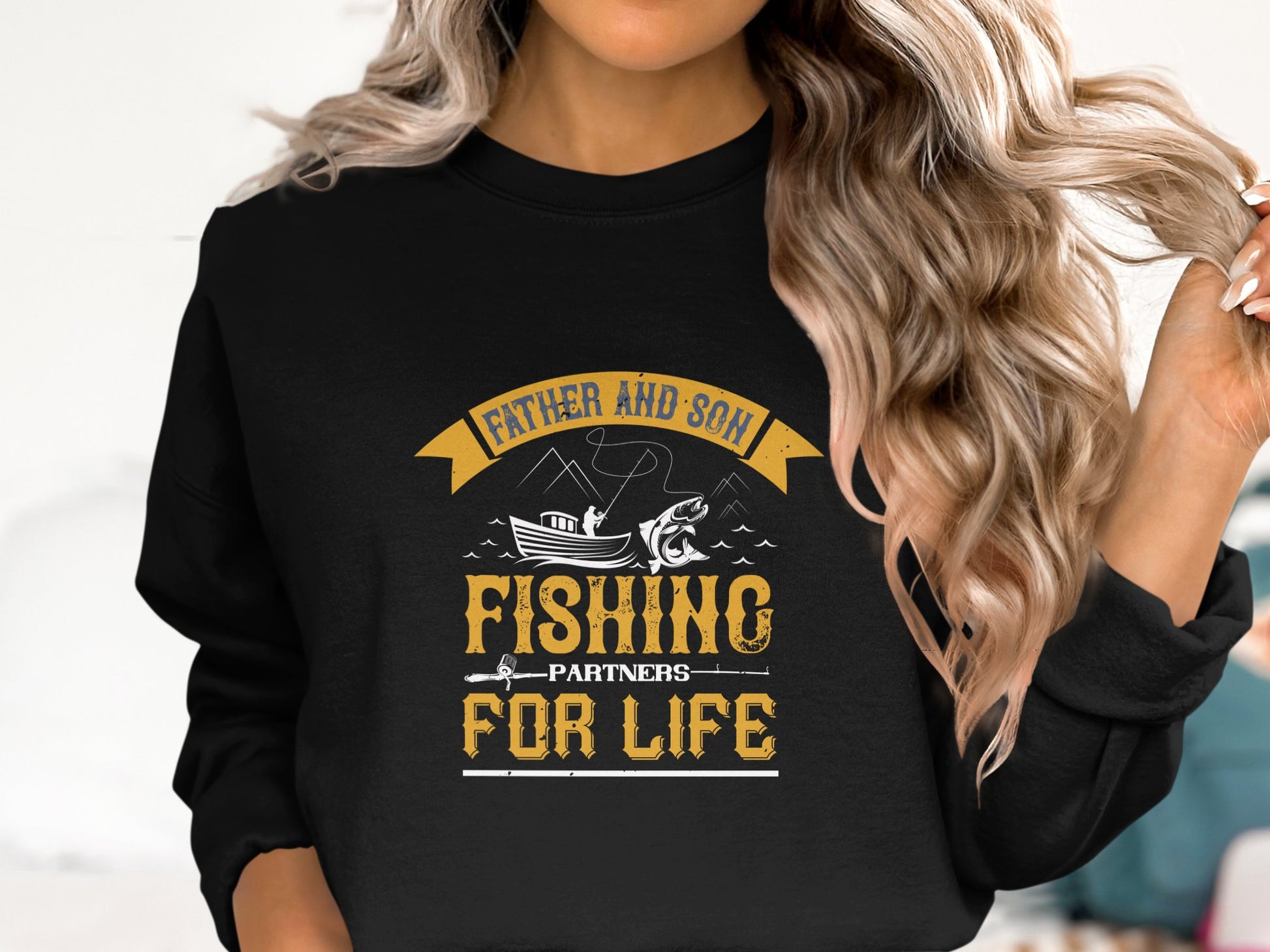 A woman with long, wavy hair wears a Garment Graphics black fishing sweatshirt featuring a boat and fish graphic with the text Father and Son Fishing Partners for Life.