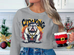 In a festive kitchen, someone holds a Santa-themed mug, wearing a Garment Graphics gray sweatshirt with a crowned bulldog and City King text. The surrounding holiday greenery and ornaments perfectly complement their stylish appearance.