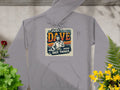 Garment Graphics graphic hoodie in medium-heavy fabric features a design of someone sitting with the text Just Dave doing Dave things. Its retro colors, paired with green ferns and yellow flowers, make it a standout piece.