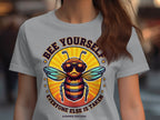 A woman wears a Garment Graphics Bee Yourself T-shirt featuring a cartoon bee with sunglasses and the words, Bee yourself, everyone else is taken. Summer Edition! This tee perfectly blends style and self-expression.