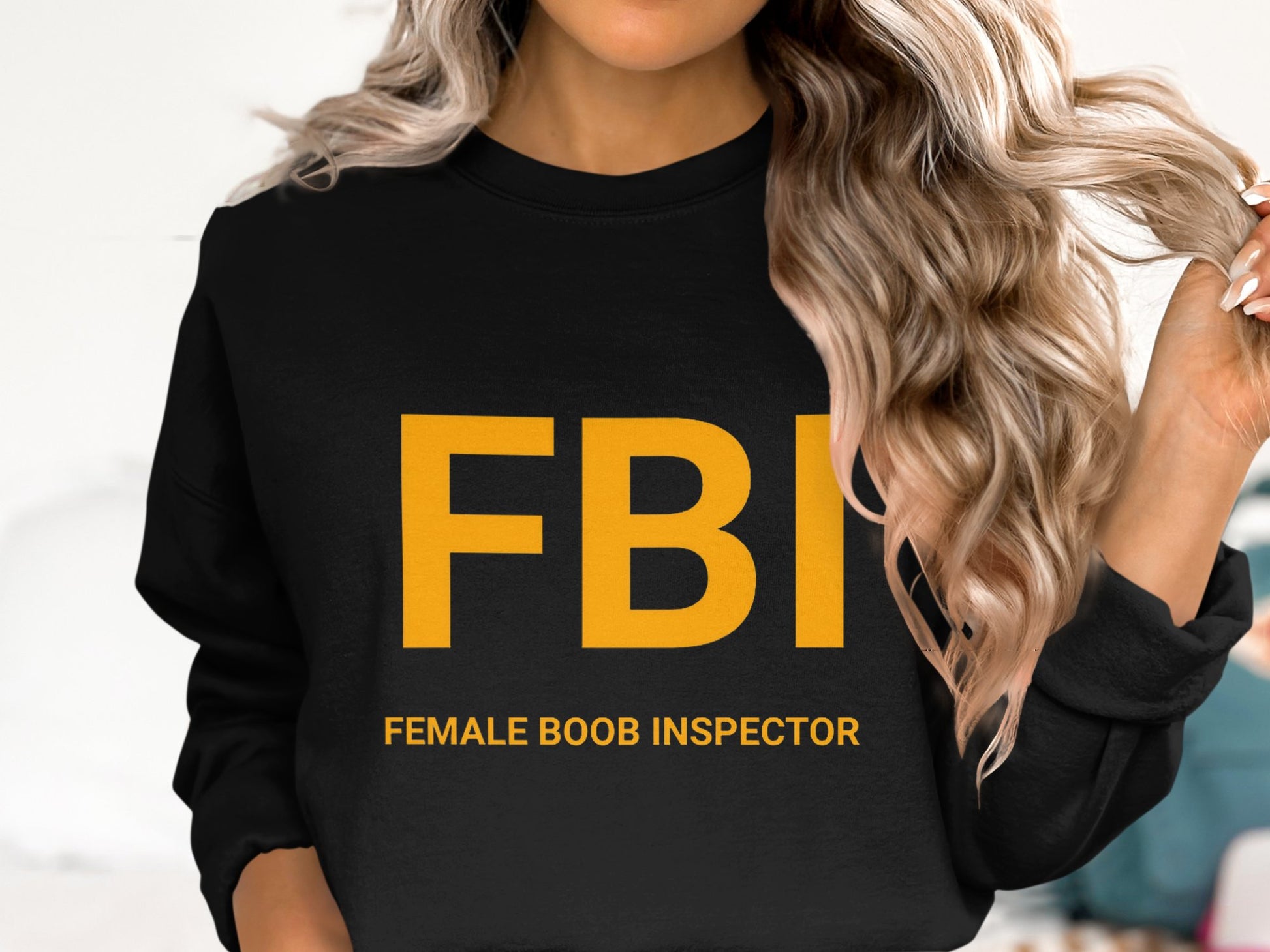 A person wears a Garment Graphics unisex graphic print sweatshirt with bold yellow FBI and Female Boob Inspector text while their long, wavy hair obscures their face.