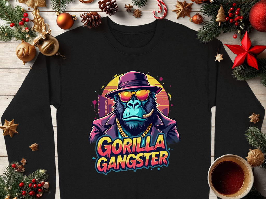 Garment Graphics black sweatshirt embodies urban style with a gorilla illustration, adorned in a hat, sunglasses, and gold chain. The Gorilla Gangster text nestles among festive Christmas decor and a warm coffee cup on wood.