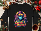 Garment Graphics black sweatshirt embodies urban style with a gorilla illustration, adorned in a hat, sunglasses, and gold chain. The Gorilla Gangster text nestles among festive Christmas decor and a warm coffee cup on wood.