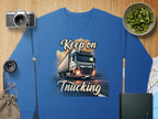 Garment Graphics presents a unisex blue graphic sweatshirt with a large truck and Keep on Trucking text. Displayed on wood with a camera, lens, sliced kiwi, book, pouch, and map for an adventure-ready vibe.