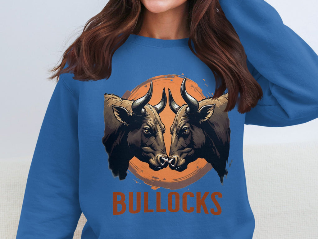An individual with long brown hair wears an eye-catching, loose fit blue sweatshirt by Garment Graphics. The design features two bulls facing each other on an orange backdrop, with BULLOCKS boldly displayed below.