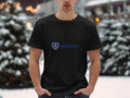 A person wearing a black Scania Logo T-shirt by Garment Graphics stands in a snowy outdoor setting. Snow-covered trees and blurred lights enhance the wintry scene, highlighting the Garment Graphics merchandise amidst natures beauty.