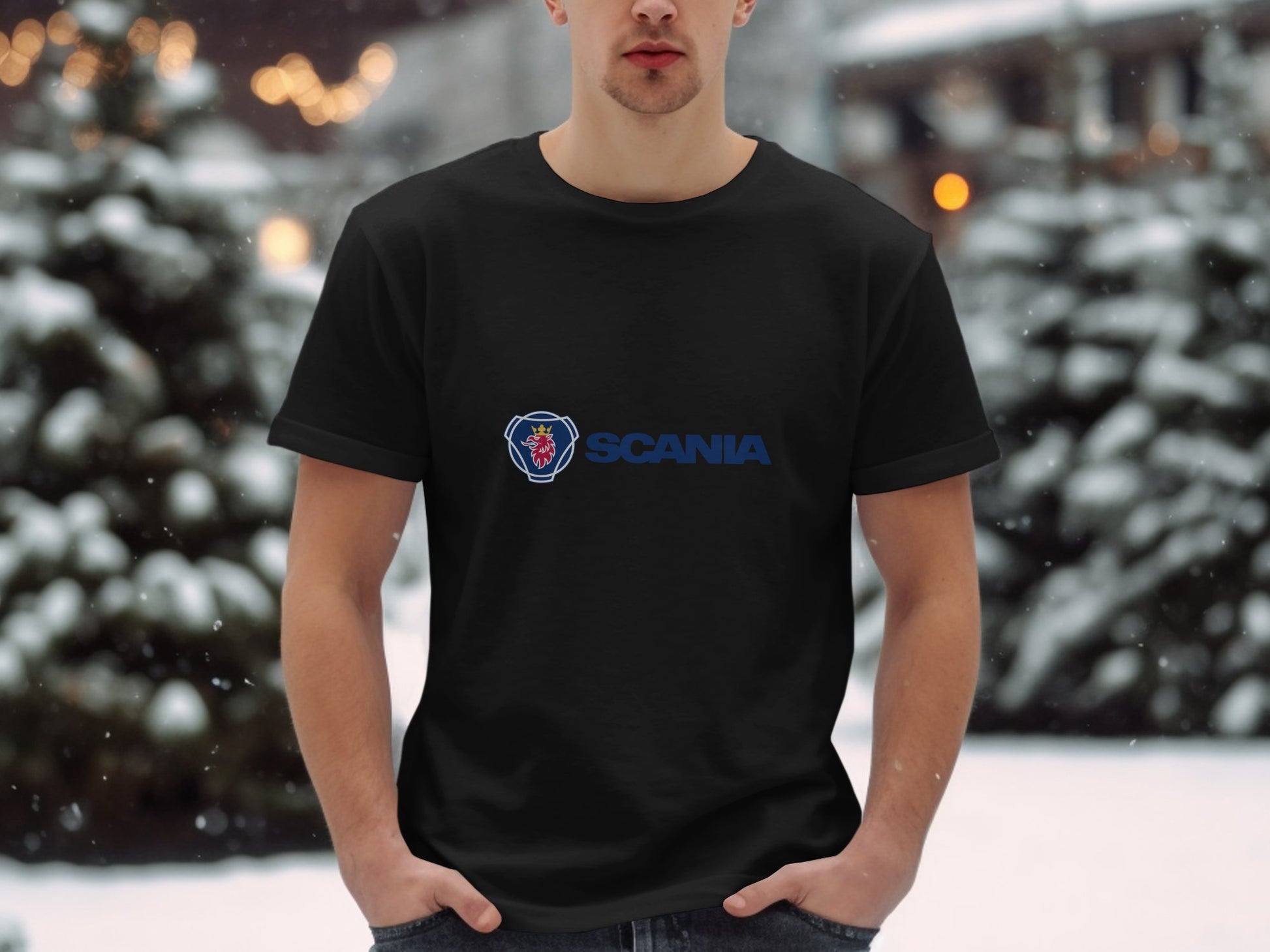 A person wearing a black Scania Logo T-shirt by Garment Graphics stands in a snowy outdoor setting. Snow-covered trees and blurred lights enhance the wintry scene, highlighting the Garment Graphics merchandise amidst natures beauty.