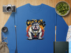 Blue CITY KING sweatshirt with bulldog and gold chain design by Garment Graphics, laid on wood with a camera, lens, fruit bowl, drawstring bag, notebook, and map.