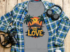 A Garment Graphics plaid blue and green shirt over a gray One Love Sunset T-shirt with palm trees. A camera, headphones, pen, and coffee cup lid sit artfully arranged on the wooden surface.