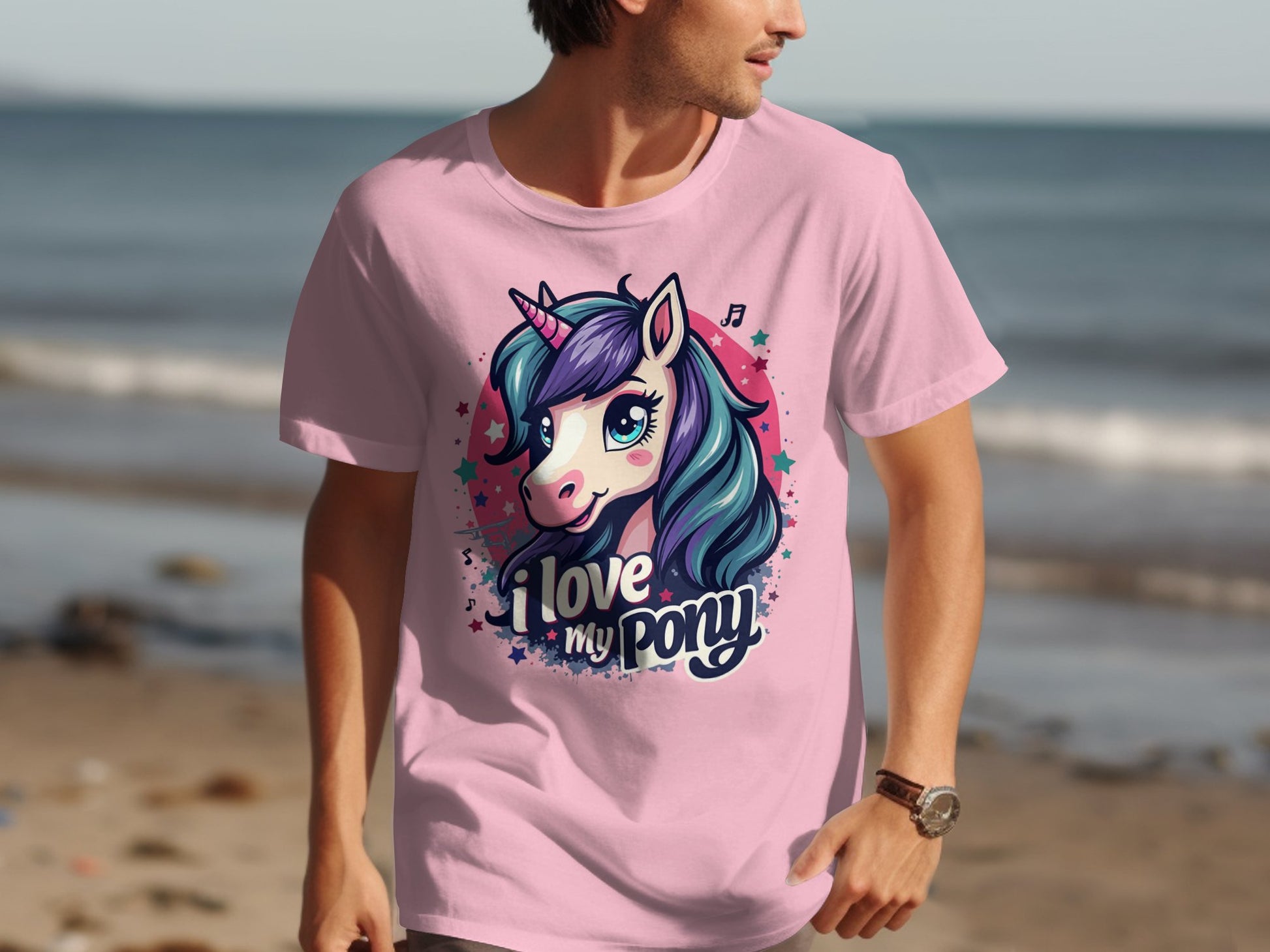A unicorn enthusiast enjoys a beach walk in a pink Garment Graphics T-shirt featuring a colorful unicorn and the phrase I Love My Pony, with the ocean and sand creating a serene backdrop.