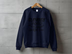 A Navy blue sweatshirt from Garment Graphics hangs on a wooden hanger against a concrete wall. It features the text Cleverly disguised as a responsible adult with an arrow design, offering unisex sizing and adding humorous charm to any wardrobe.