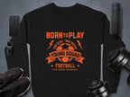 Garment Graphics black football sweatshirt features orange text and a soccer ball graphic: Born to Play, One Goal - One Dream, Young Squad, Football, Kick, Score, Celebrate! Ideal for young aspiring footballers. Unisex sizing fits all; shown with smartwatch, phone, trainers, speaker & weights.