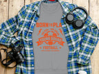 Garment Graphics offers a gray t-shirt featuring an orange and red Born to Play, One Goal, One Dream, Young Squad Football graphic. Perfect for young aspiring footballers, it pairs well with a blue plaid shirt, headphones, and a camera on a wooden surface. Unisex sizing available.