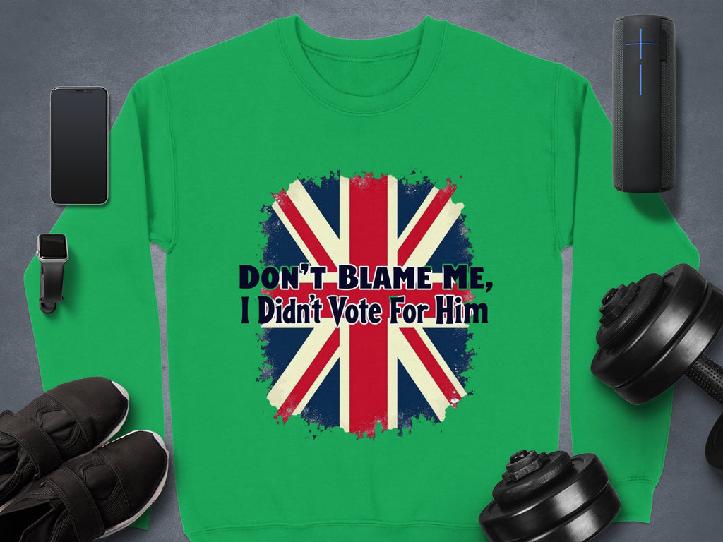 Garment Graphics offers a unisex green sweatshirt with a distressed Union Jack and DONT BLAME ME, I Didnt Vote For Him message. Displayed on gray, its surrounded by a smartphone, smartwatch, headphones, black shoes, and dumbbells.