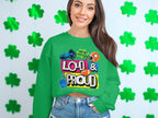 A woman stands out in a green Garment Graphics sweatshirt, featuring Hey Ho Lets Go Loud & Proud Lets Make Some Noise text with lively designs. The unisex piece is part of the Loud and Proud Sweatshirts collection. Shamrock decorations adorn the white wall behind her.