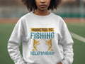 A person is outdoors in a Garment Graphics unisex fishing sweatshirt that says Addicted to Fishing Relationship with a graphic of two fish. The blurred background reveals green grass and a fence, highlighting the sweatshirts comfortable and versatile design.