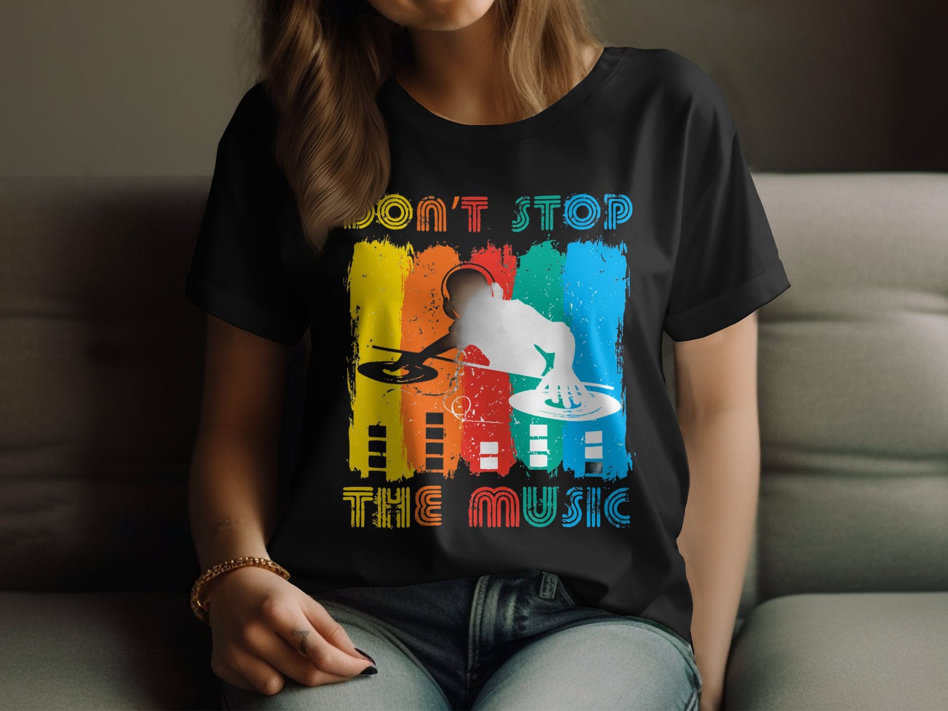 Someone relaxes on a couch wearing Garment Graphics vibrant DJ graphic tee. This black T-shirt is perfect for music lovers, with a colorful design featuring a DJ silhouette on turntables against red, yellow, and blue stripes, and the text Dont Stop the Music.
