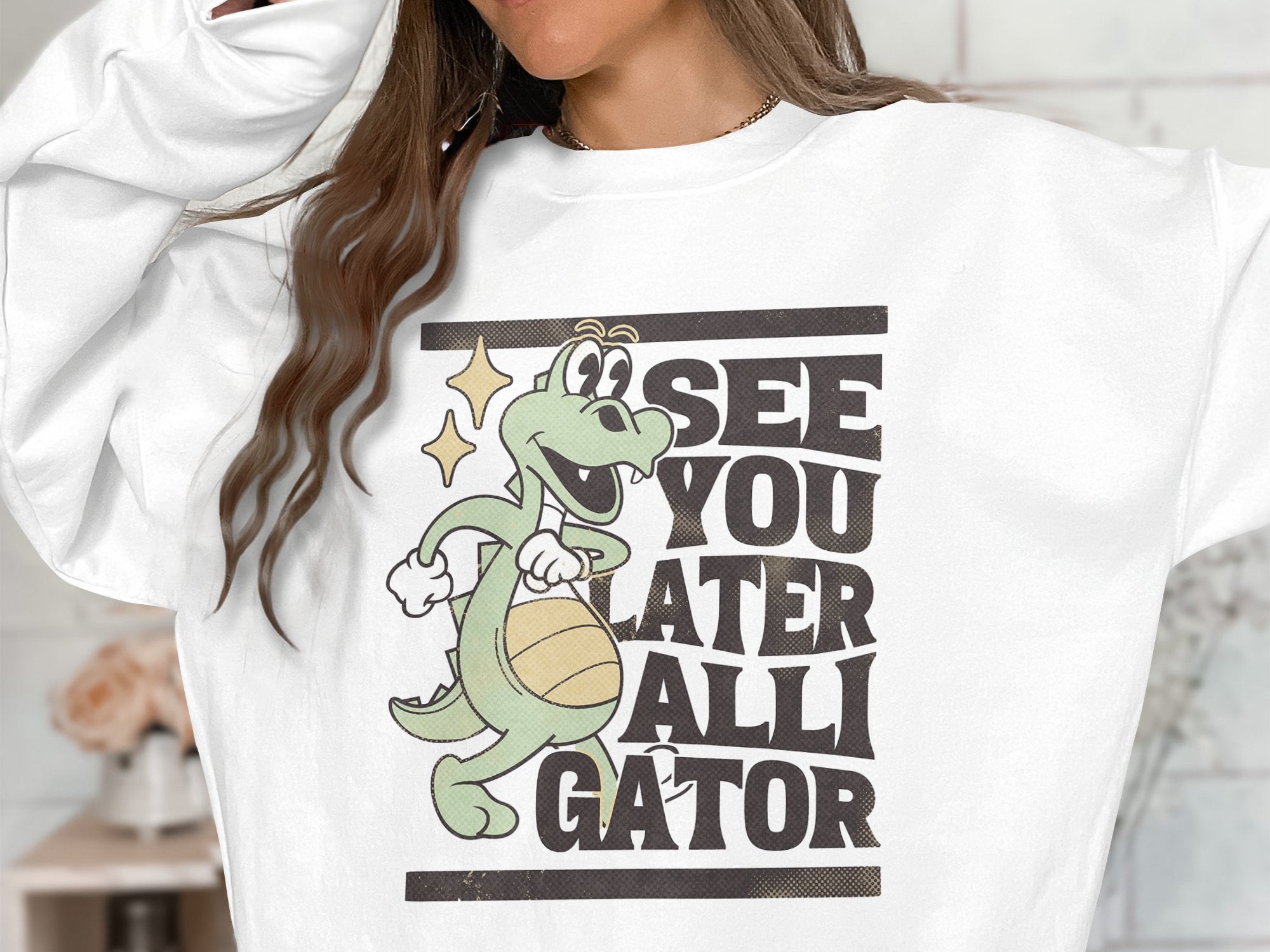 A Garment Graphics sweatshirt features a cartoon alligator with a basketball and the bold phrase SEE YOU LATER ALLIGATOR on its white fabric, with the wearers face not visible.