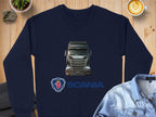 A navy blue graphic crewneck sweatshirt from Garment Graphics showcases a Scania truck image, with the logo and SCANIA in bold blue beneath it. Ideal for truck fans, its styled with a denim jacket, coffee, and potted plant on a wooden surface.