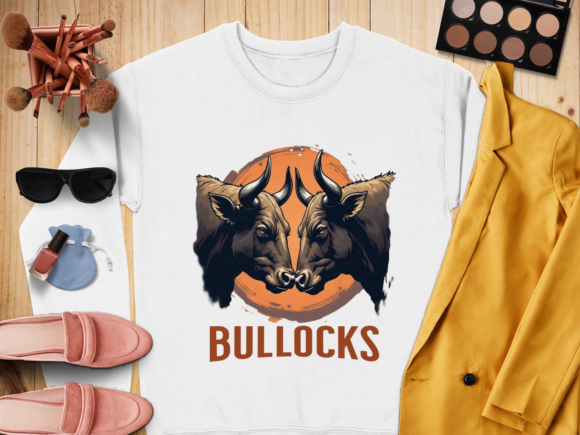 This loose-fit, white sweatshirt by Garment Graphics showcases a bold graphic of two bulls facing each other in front of an orange circle with BULLOCKS below. Perfectly paired with a yellow jacket, pink shoes, sunglasses, brushes, a powder compact, and nail polish.