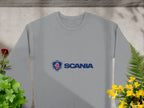 Garment Graphics gray Scania logo sweatshirt, ideal for casual outings, is displayed flat among lush greenery with red and yellow flowers framing it. Sunlight plays across the soft fabric, and its unisex sizing guarantees a comfortable fit for everyone.