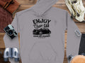 Garment Graphics offers a gray classic fit hoodie featuring a vintage car design and the text Enjoy Classic Car, Vintage Ride Community, Est. 1980, Aircooled. It embodies community spirit, surrounded by a camera, binoculars, notebooks, a bag, and a belt on wood.