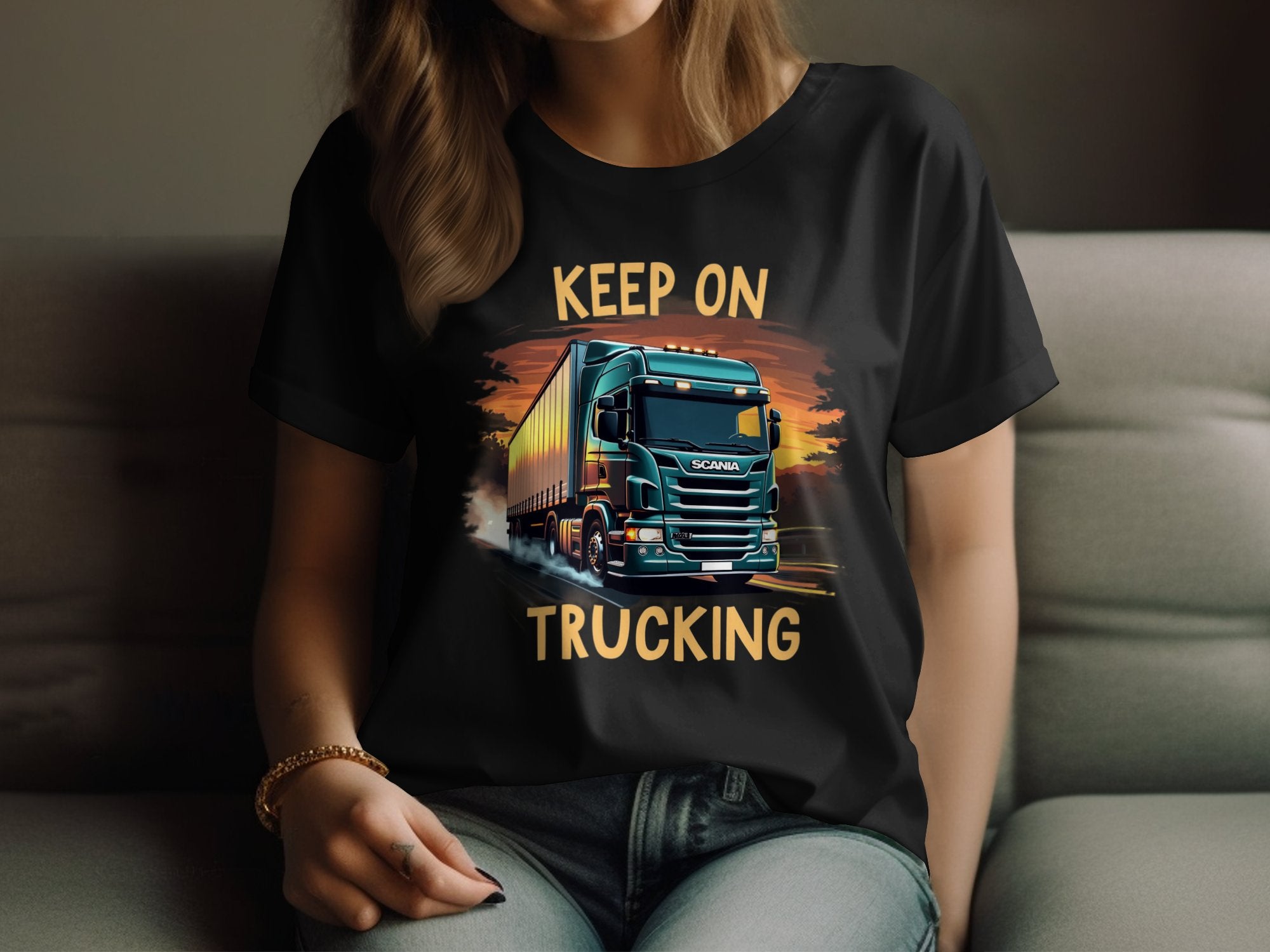 Lounging on a sofa, someone wears a black Keep on Trucking T-Shirt from Garment Graphics. This popular tee features a bold truck graphic and the phrase KEEP ON TRUCKING on a dynamic backdrop. Ideal for trucking enthusiasts, their face remains unseen.