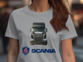 A person with long brown hair wears a gray Garment Graphics T-shirt featuring a detailed illustration of a Scania truck on the front. Ideal for automotive enthusiasts, this graphic tee prominently displays the Scania logo and name in blue below the truck.