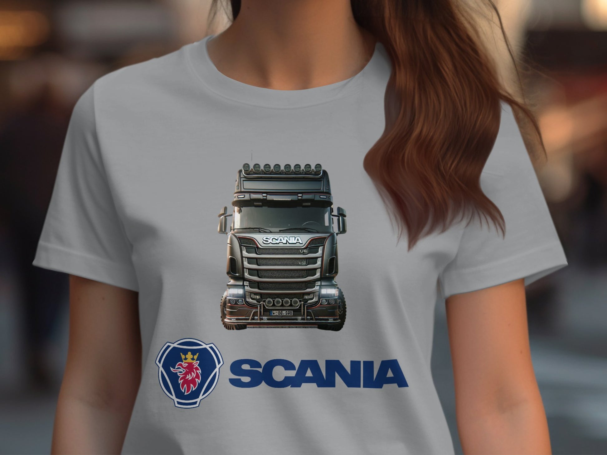 A person with long brown hair wears a gray Garment Graphics T-shirt featuring a detailed illustration of a Scania truck on the front. Ideal for automotive enthusiasts, this graphic tee prominently displays the Scania logo and name in blue below the truck.
