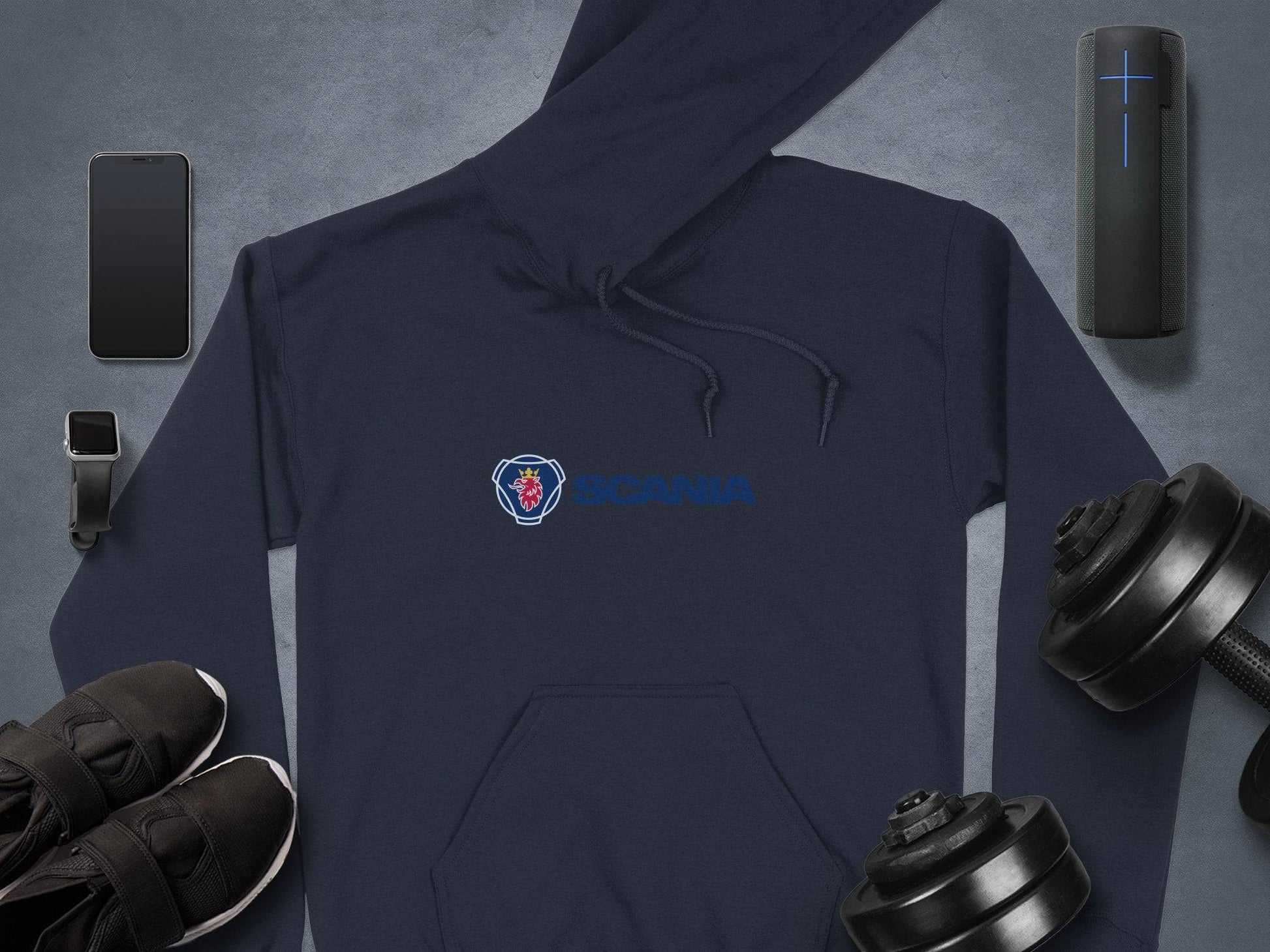 A dark blue Garment Graphics hoodie with the iconic logo is on a gray surface, surrounded by a smartphone, smartwatch, wireless speaker, black shoes, and two dumbbells.