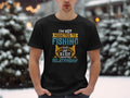 In a snowy setting, a person wears a black Garment Graphics Fishing T-shirt featuring a colorful design with the text: Im not addicted to fishing, we are just in a very committed relationship, ideal for devoted anglers.