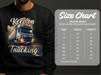 A man wears a Garment Graphics black sweatshirt featuring a truck illustration and Keep on Trucking. A Gildan 18000 size chart (S to 5XL) is beside him, ideal for those embracing the open road.
