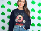 A woman in a Garment Graphics navy sweatshirt with a quirky donut character, ears, and gloves stands before a green clover wall. Her long brown hair falls over her jeans. The sweatshirts unisex sizing offers the perfect fit for everyone.
