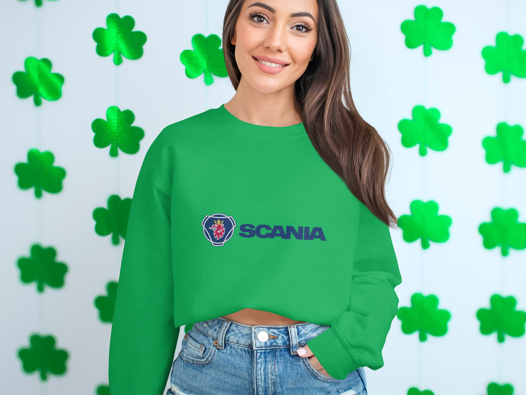 Wearing a green Garment Graphics Scania logo sweatshirt with unisex sizing, the person smiles against a shamrock backdrop. With long brown hair and denim shorts, theyre perfectly dressed for casual outings.