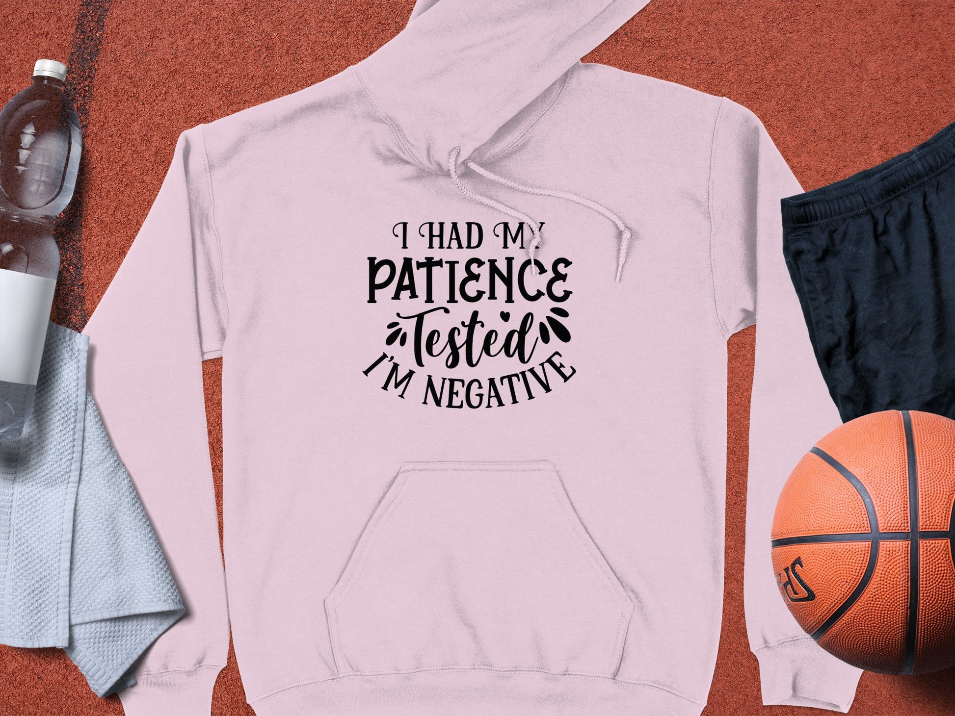 A novelty pink hoodie from Garment Graphics, featuring I had my patience tested Im negative lies on the gym floor with a basketball, black shorts, towel, bottled drink, and white phone—ideal for fans of comedic statement hoodies.