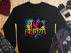Garment Graphics presents a black sweatshirt with bold I Love Graffiti text in vivid graffiti-style letters. Splashes of blue and red paint over yellow brick wall motifs create an urban vibe, ideal with a hat, gloves, and plaid clothing on a wooden backdrop.