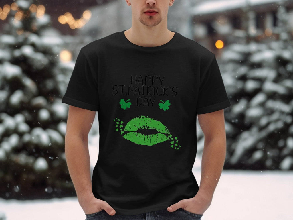 A person stands outside in the snowy landscape wearing a Garment Graphics T-shirt featuring festive green lips and clovers with the phrase Happy St. Patricks Day. Snow-laden trees and soft, blurred lights enhance the magical scene.