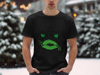 A person stands outside in the snowy landscape wearing a Garment Graphics T-shirt featuring festive green lips and clovers with the phrase Happy St. Patricks Day. Snow-laden trees and soft, blurred lights enhance the magical scene.