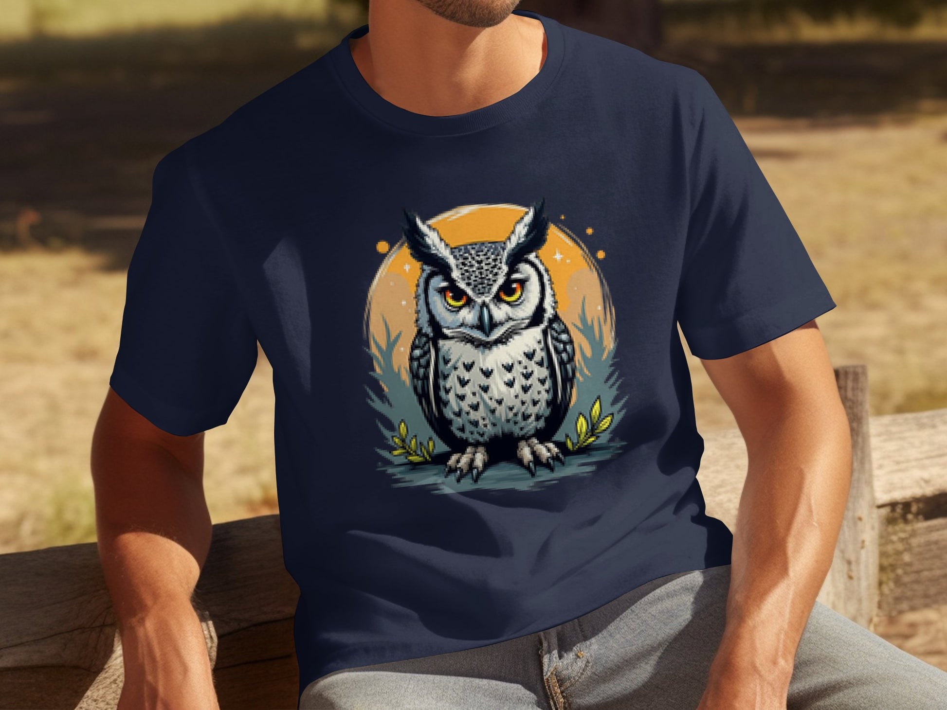 A person in a Garment Graphics navy blue T-shirt featuring an intense owl graphic against an orange circular backdrop with foliage accents sits artistically on a wooden bench outdoors.
