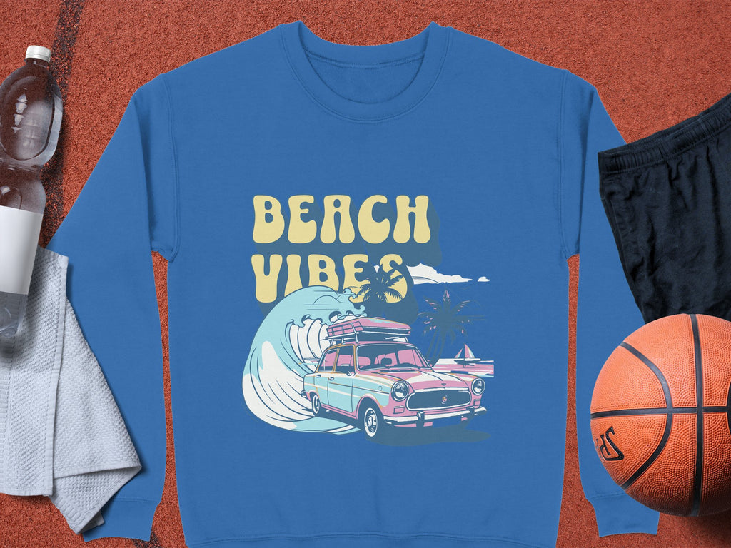 Garment Graphics blue sweatshirt showcases a vintage car, surfboards, a big wave, palm trees, and BEACH VIBES in yellow. This retro road trip design stands out on a textured brown background and pairs well with basketball gear like black shorts and a water bottle.